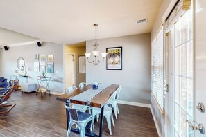 A dining area with a wooden table and chairs, a chandelier, and framed pictures on the wall. - The Brick Beauty | Dog-Friendly & Fenced Yard (Bentonville)