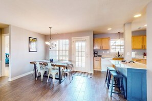 A spacious kitchen with a dining area, wooden cabinets, and a blue island. - The Brick Beauty | Dog-Friendly & Fenced Yard (Bentonville)