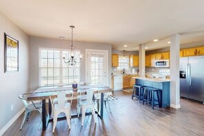 A modern kitchen with a dining area, wooden cabinets, stainless steel appliances, and a chandelier. - The Brick Beauty | Dog-Friendly & Fenced Yard (Bentonville)