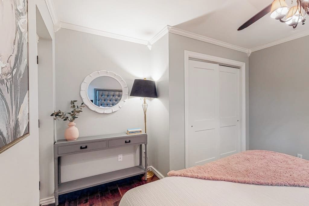 Une chambre à coucher avec un lit, une coiffeuse avec un miroir, une lampe et une porte.