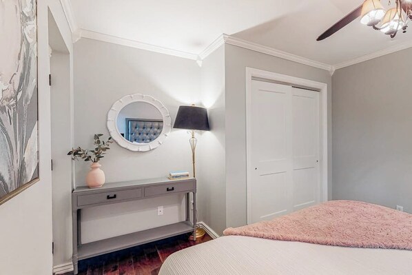 Un dormitorio con una cama, un tocador con espejo, una lámpara y una puerta.