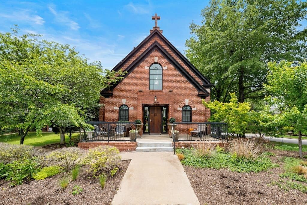 A brick church with a cross on top, a front entrance, and a paved walkway leading to it.