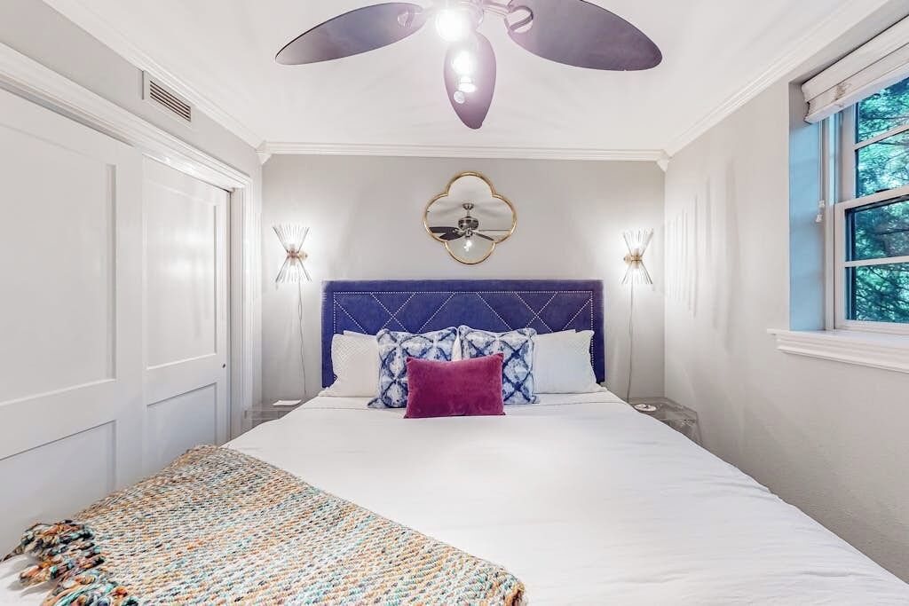 A bedroom with a bed, a ceiling fan, a wall clock, and a window.