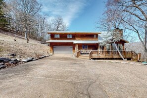 A two-story wooden cabin with a garage, a deck, and a stone chimney. - Lakefront 6BR with infinity pool, sauna & kayaks (Rogers)