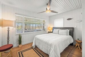 A bedroom with a bed, a ceiling fan, a window with blinds, a lamp, and a small table with a plant. - 2BR Sunroom Charm & Lakefront Dock Living (Hot Springs)
