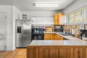 A kitchen with a stainless steel refrigerator, wooden cabinets, a granite countertop, and a sign prohibiting smoking or vaping. - 2BR Sunroom Charm & Lakefront Dock Living (Hot Springs)