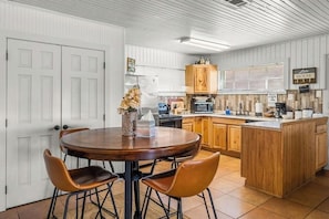 Een keuken met een houten kookeiland, witte kasten en een eethoek met een ronde tafel en stoelen.