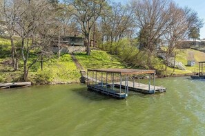 A riverside dock with a covered seating area, surrounded by trees and a grassy embankment. - 2BR Sunroom Charm & Lakefront Dock Living (Hot Springs)