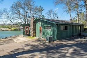A small, single-story building with a stone foundation and green siding, located near a body of water. - 2BR Sunroom Charm & Lakefront Dock Living (Hot Springs)
