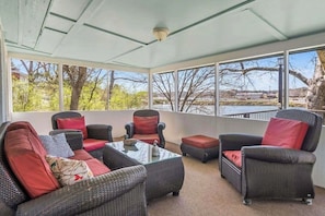 A sunroom with wicker furniture, a glass coffee table, and a view of a lake. - 2BR Sunroom Charm & Lakefront Dock Living (Hot Springs)
