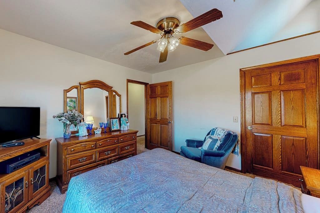 Ein Schlafzimmer mit Bett, Kommode, Fernseher und Deckenventilator.