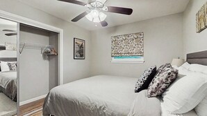 Un dormitorio con cama, ventilador de techo, armario y ventana con vistas.