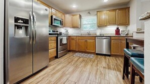 Una cocina con refrigerador de acero inoxidable, microondas, horno, lavavajillas, gabinetes de madera y encimera de granito.