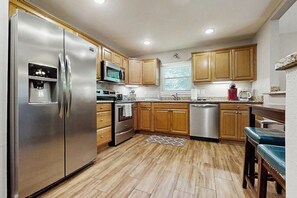 A kitchen with a stainless steel refrigerator, microwave, oven, dishwasher, wooden cabinets, and a granite countertop. - 3BR Inviting woodland retreat - direct bike trail (Bella Vista)