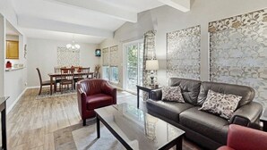Una sala moderna con un sofá de cuero, una mesa de centro de vidrio y un comedor con una mesa y sillas de madera.