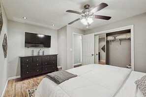 Een slaapkamer met een bed, een dressoir, een plafondventilator, een televisie en een inloopkast.
