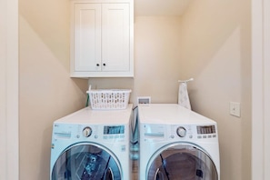 A laundry room with two front-loading washing machines, a white cabinet above, and a basket on the top of the left machine. - Downtown Bentonville Condo - Secure Bike Storage (Bentonville)