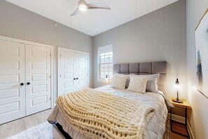 Ein Schlafzimmer mit einem Bett, einem Nachttisch, einer Lampe, einem Fenster und einer Tür.