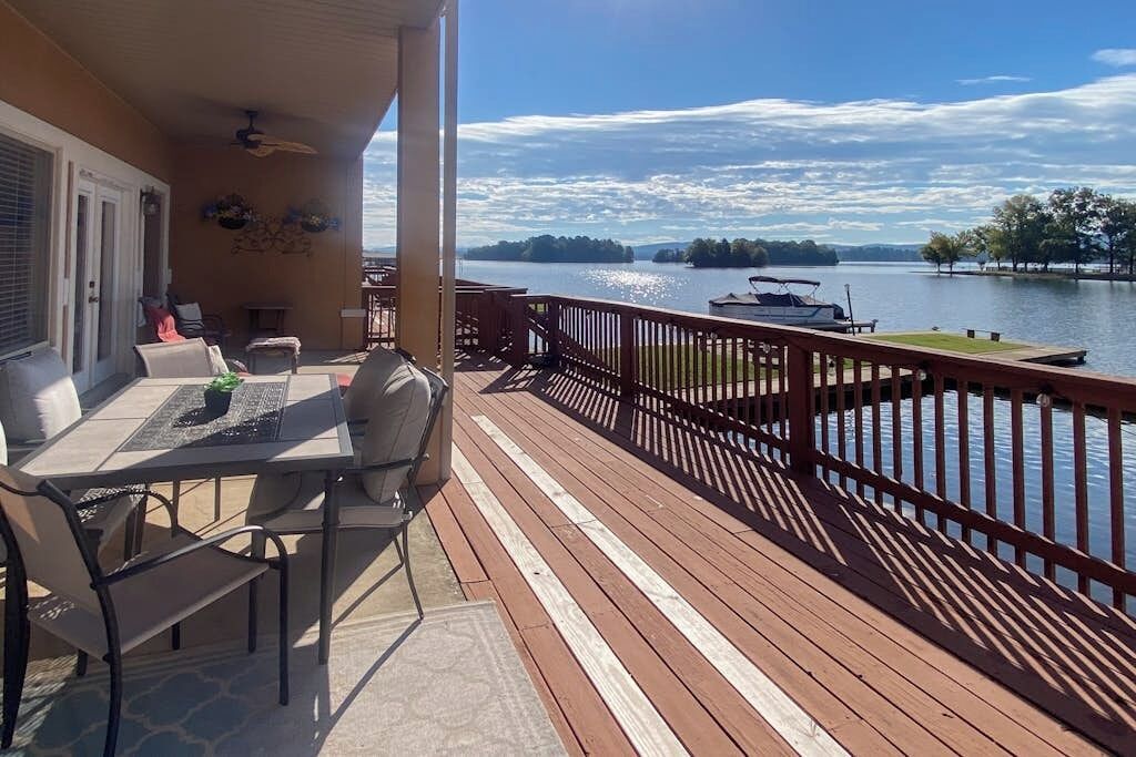 Varanda com mesa e cadeiras, com vista para um lago com barcos e um píer.