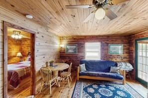 L’intérieur d’une cabine avec un plancher en bois, une table à manger ronde entourée de chaises, un canapé et un ventilateur de plafond.