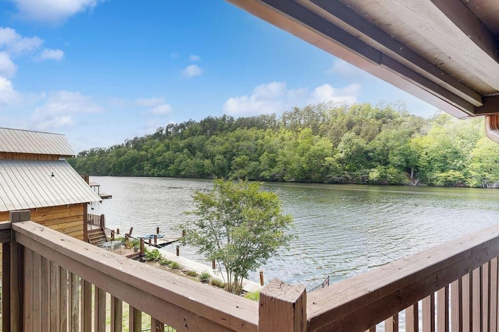 A wooden deck overlooking a lake with a forested hillside in the background.