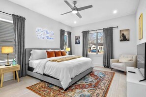 Una camera da letto moderna con un letto grande, un ventilatore a soffitto, una TV e vista sull'esterno.