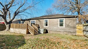 Une maison de plain-pied avec une terrasse à l’avant, un escalier en bois et une cour clôturée.