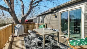 Une terrasse extérieure avec une table et des chaises, un barbecue couvert et une grande porte-fenêtre coulissante donnant sur un patio abrité.