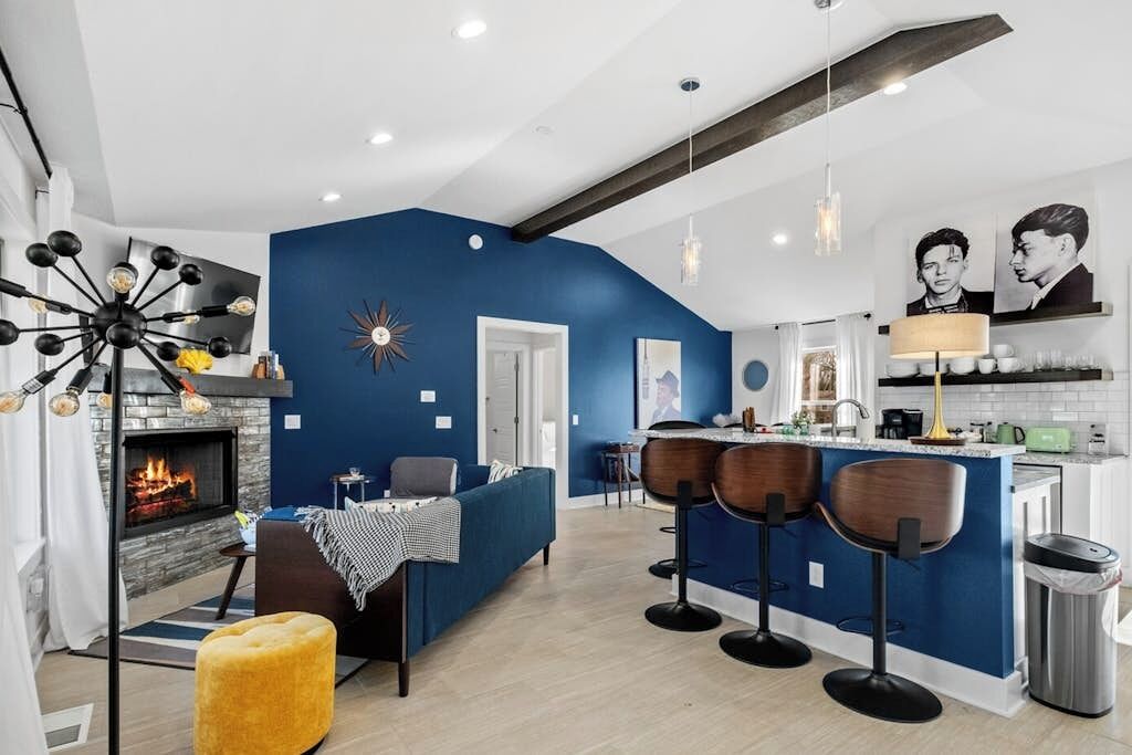 A modern kitchen with a blue accent wall, a built-in bar area with stools, a fireplace, and a ceiling with exposed beams.