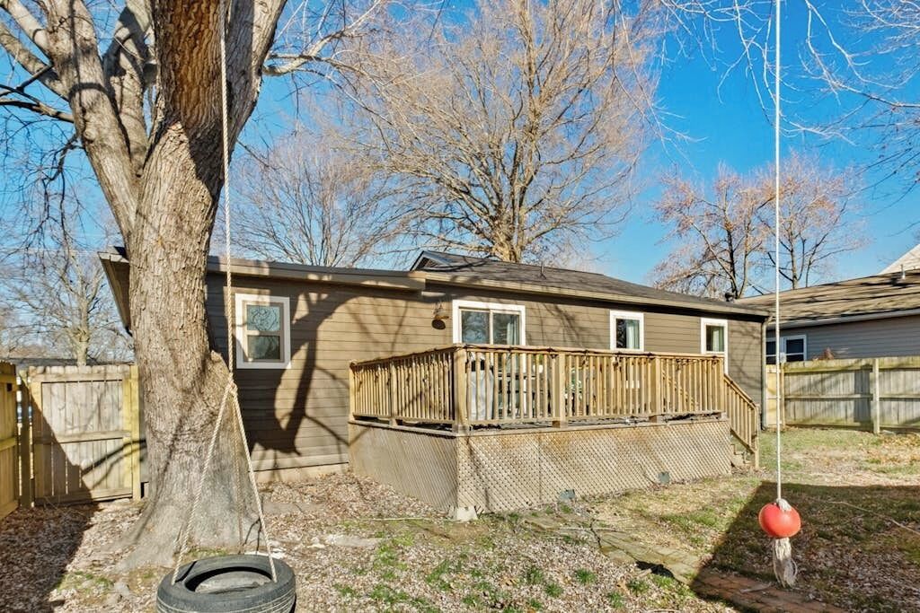 A residential house with a wooden deck, a swing hanging from a tree, and a tire swing on the ground.