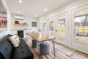A modern kitchen with a dining table, a black sofa, and a large window. - B Street Bungalow | Bike-In/Bike-Out & Game Room (Bentonville)