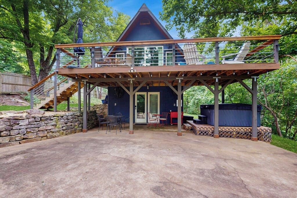 Une cabane en bois à deux étages, dotée d’un balcon, d’un mur en pierre et d’un espace extérieur aménagé pour s’asseoir.