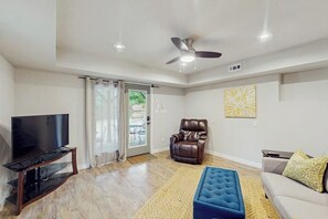 A living room with a flat-screen TV, leather chair, sofa, and a ceiling fan. - 2BR dog-friendly cottage with spa & boat parking (Rogers)