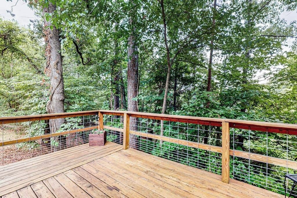 A wooden deck with a wire fence, surrounded by dense green foliage.