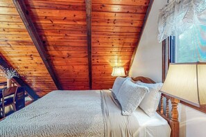 Ein Schlafzimmer mit Holzboden, einem Bett mit weißer Bettwäsche, einem Nachttisch und einem Fenster mit Spitze.
