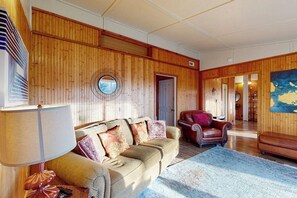 A room with a wooden paneled wall, a round mirror, a sofa with patterned cushions, a red leather armchair, and a large rug. - Quiet 2BR Lakeview Dog Friendly - Deck - Firepit (Eureka Springs)