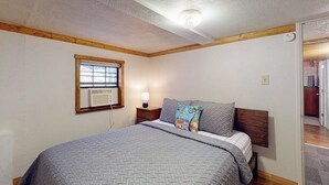 A bedroom with a single bed, a nightstand, a lamp, a window with an air conditioner, and a door leading to another room. - Quiet 2BR Lakeview Dog Friendly - Deck - Firepit (Eureka Springs)