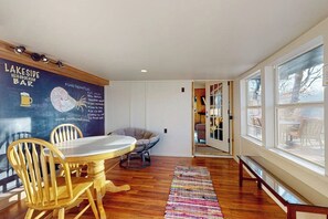 Ein Zimmer mit Esstisch, Stühlen, einem bunten Teppich und einer Tafelwand mit Text und Zeichnungen.