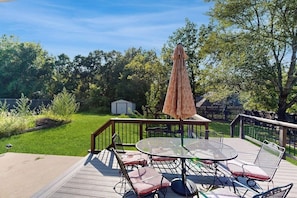 A deck with a round table and chairs, surrounded by a wooden deck and a metal railing. - Bella Vista Retreat | Bike-In/Out & Game Garage (Bella Vista)