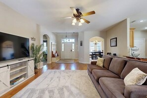 A living room with a flat-screen TV, a ceiling fan, a brown sofa, and a large rug.