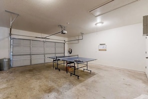 A garage with a ping pong table, a garage door, and a wall-mounted electrical panel. - Bella Vista Retreat | Bike-In/Out & Game Garage (Bella Vista)