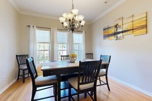 A dining area with a wooden table, four chairs, a chandelier, and a window with curtains.