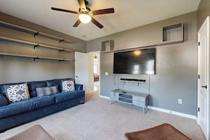 A living room with a blue sofa, a flat-screen TV mounted on the wall, a ceiling fan, and a staircase leading to another room. - Bella Vista Retreat | Bike-In/Out & Game Garage (Bella Vista)