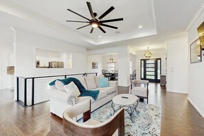A spacious living room with a white sofa, a coffee table, and a ceiling fan. - Lake Brittany Lodge | Lake View, Deck & Firepit (Bella Vista)