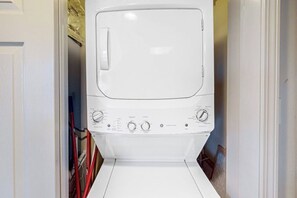 Lavadora blanca en un cuarto de lavado, con perillas de control visibles y una puerta.