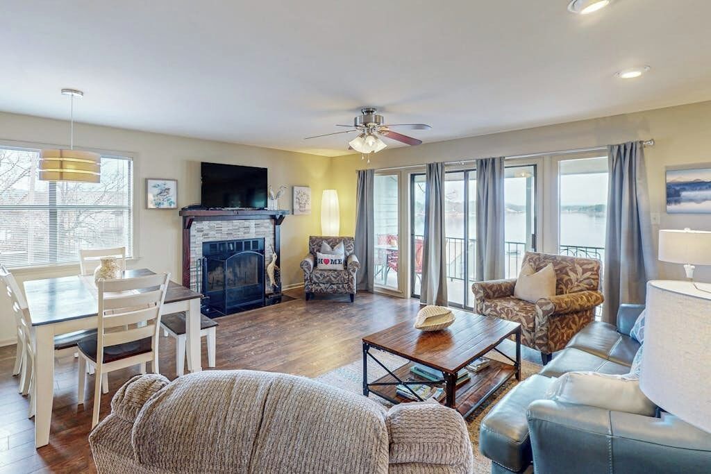 A living room with a fireplace, a ceiling fan, a dining area with a table and chairs, and a sofa.