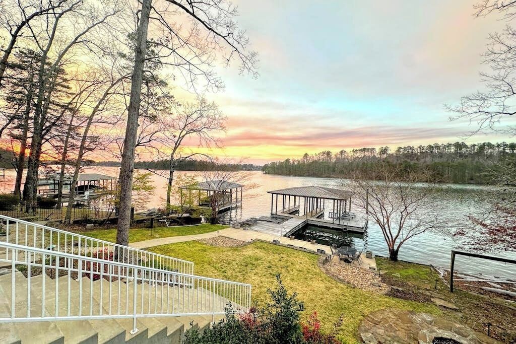 A lakeside property with a dock, covered seating areas, and a staircase leading to a deck.