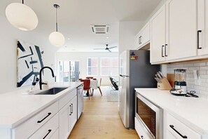 A modern kitchen with white cabinetry, a built-in oven, and a dining area with a table and chairs. - 2BR Modern Townhouse with Balcony (Bentonville)