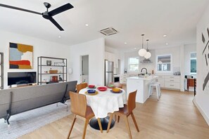 A modern kitchen with white cabinetry, a dining area with a round table, and a ceiling fan. - 2BR Modern Townhouse with Balcony (Bentonville)