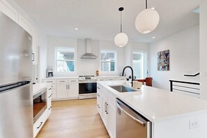 A modern kitchen with white cabinetry, a central island, stainless steel appliances, and pendant lighting. - 2BR Modern Townhouse with Balcony (Bentonville)